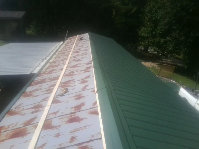 Old rusted panels beside newly installed green metal roofing — Wind Damage Roof Repair by Roofing Brothers in Silver Star